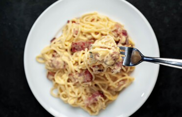 Homemade carbonara pasta in a white plate on a stone background