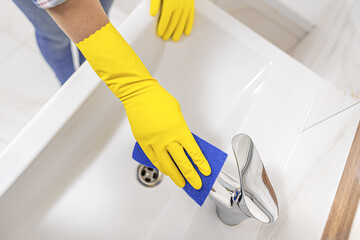 Cleaning in the bathroom. A woman wipes the sink and washbasin faucet.