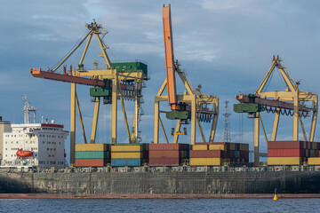Container ship at unloading in a cargo port. The cargo ship is unloaded by crane.