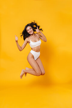 Image of young happy woman in swimsuit jumping and showing thumbs up