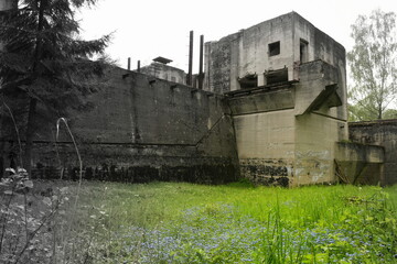 Fototapeta na wymiar A semi black and white photo of the exterior of an old dilapidated dam built by the Nazis during World War Two with a lush meadow full of flowers and herbs in the foreground seen on a spring day
