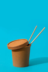 Craft takeaway food container with chopsticks on a blue background. Delivery food.