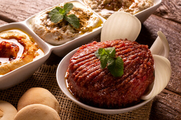 Raw quibe garnished with mint, Hummus, baba ganoush, onion and bread.