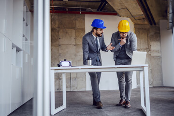 Two dedicated hardworking architects standing in building in construction process and working on improvement of blueprints.