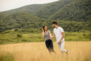 Naklejka na ściany i meble Happy young couple in love walking through grass field