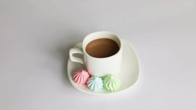 Multicolored meringuesand a cup of coffee on a white background