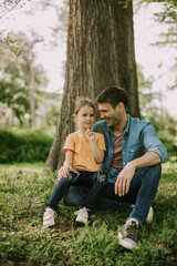 Single father sitting on grass by the tree with little daughter