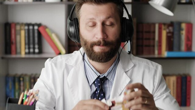Otolaryngologist talking to camera. Attractive bearded cardiologist in white coat explains something while looking at camera using model of human ear as example