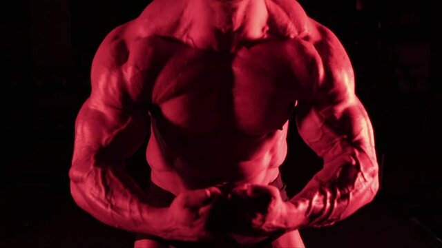 posing muscular bodybuilder in red light with a dark background