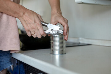 A woman in the kitchen opens a can. Hand open canned food in metal can. Close up canned goods non perishable food storage goods in kitchen home