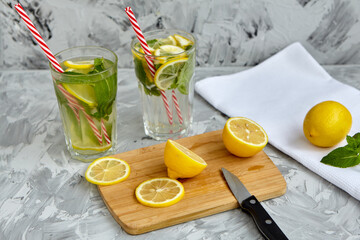 The process of making lemonade. On a wooden Board is a Lemon and mint next to a knife. There are glasses of lemonade in the background. Summer drink. Lemonade with lemon and mint. Selective focus