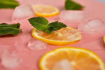 Composition with cut citrus fruits on pink background. Creative summer background composition with lemon slices, leaves mint and ice cubes. Minimal top down lemonade drink concept.Top view