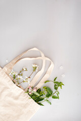 Zero waste shopping concept - cotton bag, glass bottle for water with spring flowers, herbs and leaves on a light background.