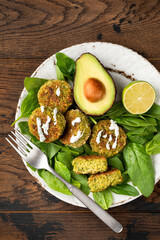 Vegetarian falafel with avocado and spinach on plate, wooden table background, top view