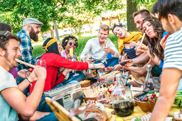 Happy friends having fun outdoor eating snack and drinking red wine at bbq picnic - Young multiracial people enjoying summer time together at barbecue garden party - Friendship concept on vivid filter