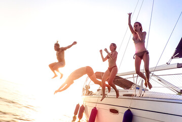 Young millenial friends jumping from sailboat at sea ocean trip - Guys and girls having summer fun...
