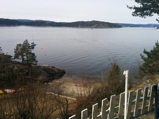 Calm view of the seaside with trees and small boats behind a white fence