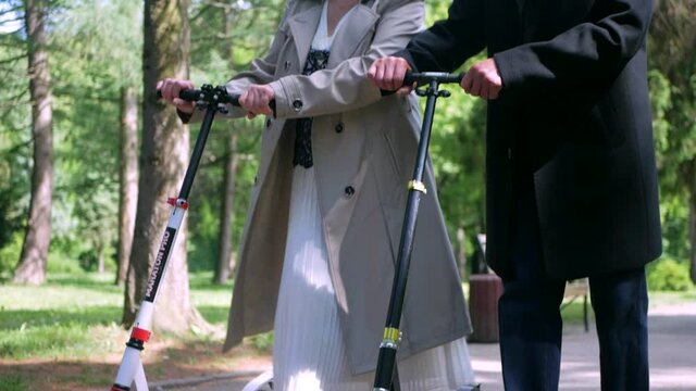 Loving old couple walking in the park. Grandparents ride scooters. Beautiful old man and happy old woman.