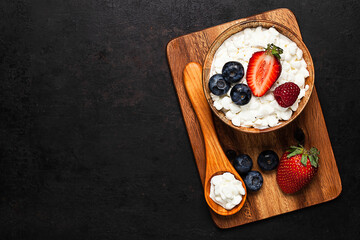 top view on wooden bowl with cottage cheese and berries standing on wooden board. placed on old rustic background