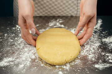 Woman in checkered apron preparing the dough on stainless steel kitchen table.