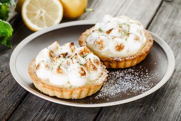 Two tasty lemon Meringue Tartlets with mint  on plate standing on old wooden table