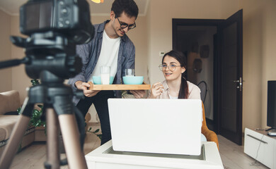 Brunette teacher with eyeglasses having an online lesson while her husband brings her breakfast