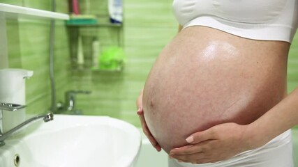 pregnant girl lubricates stomach with cream against stretch marks in the bathroom