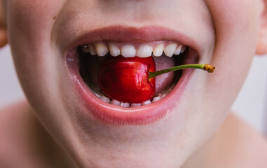 Obraz premium The child holds a delicious cherry in his mouth. Beautiful red berry. The child smiles.