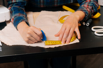 A seamstress girl measures the length on the fabric. The craftsman draws a tailor small. The...