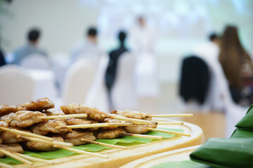 cooked grilled roasted pork sticks are arranged on the banana leaf behind the seminar / training...
