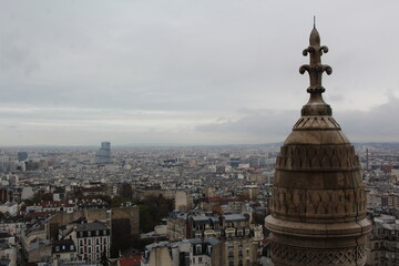 Basilica dome spire close up with Paris city skyline in the background against a gloomy grey cloudy...