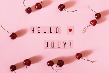 Hello July text and and cherry berry scattering on pink background. Hello July concept