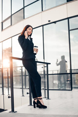 Successful smiling businesswoman or entrepreneur talking to the phone standing in front of his office.