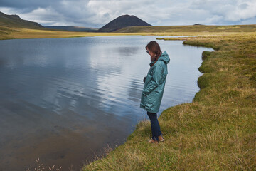 Fototapeta na wymiar A girl takes a picture of a mountain lake by phone. Iceland.