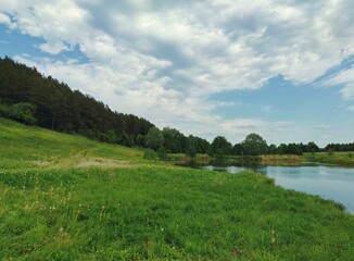 Fototapeta na wymiar beautiful blue sky with clouds before the rain over a green meadow between the forest and the lake