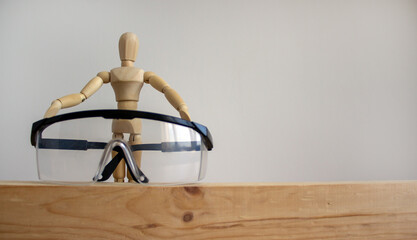 Safety glasses on a wooden bar. Wooden model of human. Beautiful white background. Copy space.