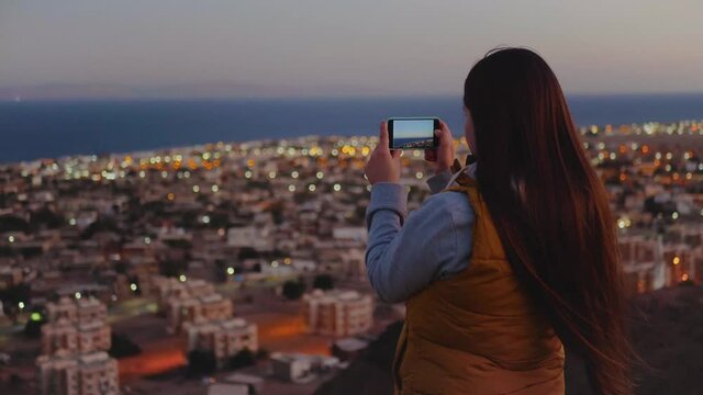 Woman take picture of the sea by smartphone in the evening. Woman stay on top of the mountain and looking Into Horizon, 4k
