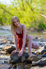 girl in a red dress sits on the shore of a mountain river
