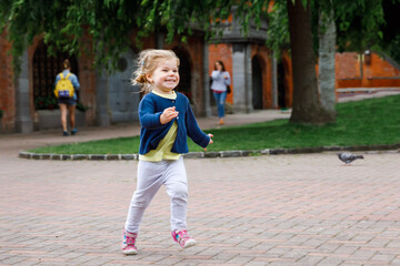 Cute little happy toddler girl running in park in Dublin, Ireland. Smiling and laughing baby child having fun spending family vacations in nature. Traveling with small kids