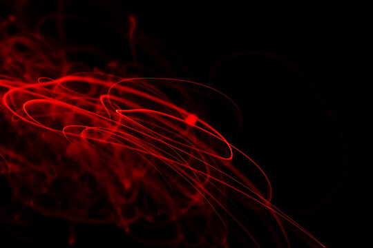 Long exposure light painting photography, curvy lines of vibrant neon ruby red in loop against a black background with blank space. Neon light painting.