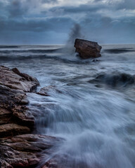 Rough Sea and brooding, stormy sky over Charlies Garden, rock pillar at Seaton Sluice on the coast of Northumberland, England, UK.