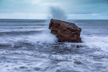 Rough Sea and brooding, stormy sky over Charlies Garden, rock pillar at Seaton Sluice on the coast of Northumberland, England, UK.