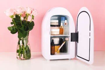 Mini fridge on pink background. Minimal composition. Trendy beauty item to keep skincare and makeup products cool and fresh.