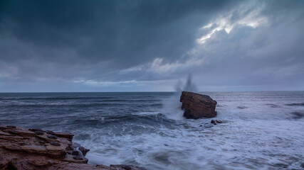 Rough Sea and brooding, stormy sky over Charlies Garden, rock pillar at Seaton Sluice on the coast...