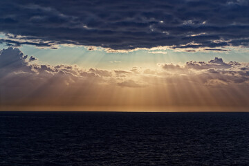 Sunbeams and dark clouds over sea during sunset