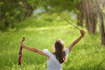 Woman Outdoor,Beautiful romantic girl with dark hair and white dress playing on a violin in spring park. Photo of sensual woman in glowing sun. © saravut