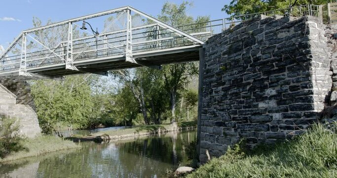 Beautiful, historic, pedestrian bridge, over gently flowing creek, blue sky, wispy rolling clouds