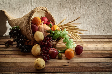 Thanksgiving cornucopia filled with pumpkins and fruit decorated with flower against a rustic...