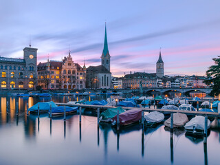 Skyline of historical buildings on the west bank of the Limmat river in Zurich, Switzerland, reflected on the water under a blue and pink sky