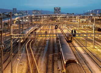 Lit train tracks at the blue hour,  near a busy railway station